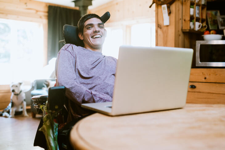 Smilende gutt i rullestol jobber på pc